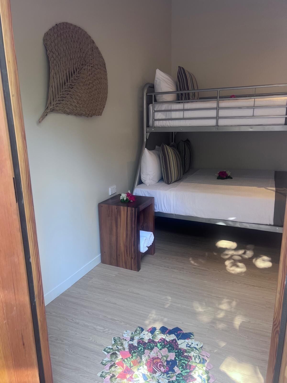 A compact bedroom with a bunk bed, a small wooden side table, and a woven wall hanging.