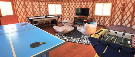 A room with a ping pong table, foosball table, and a pool table.