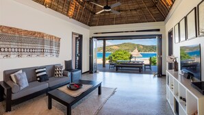 Un salon moderne comprenant un canapé, une table basse et un téléviseur, donnant sur un balcon avec vue sur la plage et l’océan.