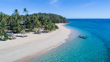 Relax on a wide sandy beach with clear waters, shaded by palm trees and a thatched-roof hut.