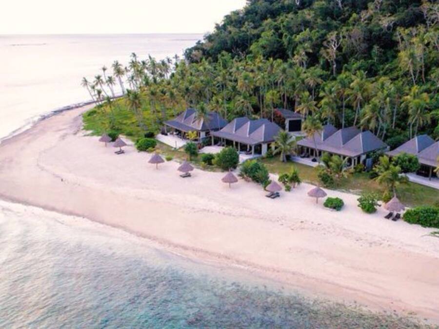 A beachfront resort with multiple overwater bungalows, a sandy beach, and lush greenery.