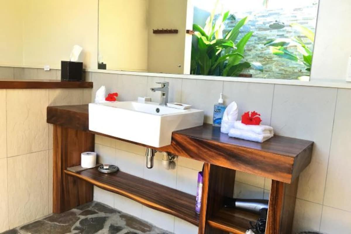 Un baño con tocador de madera, un lavabo blanco, un espejo y vistas a la vegetación a través de la ventana.