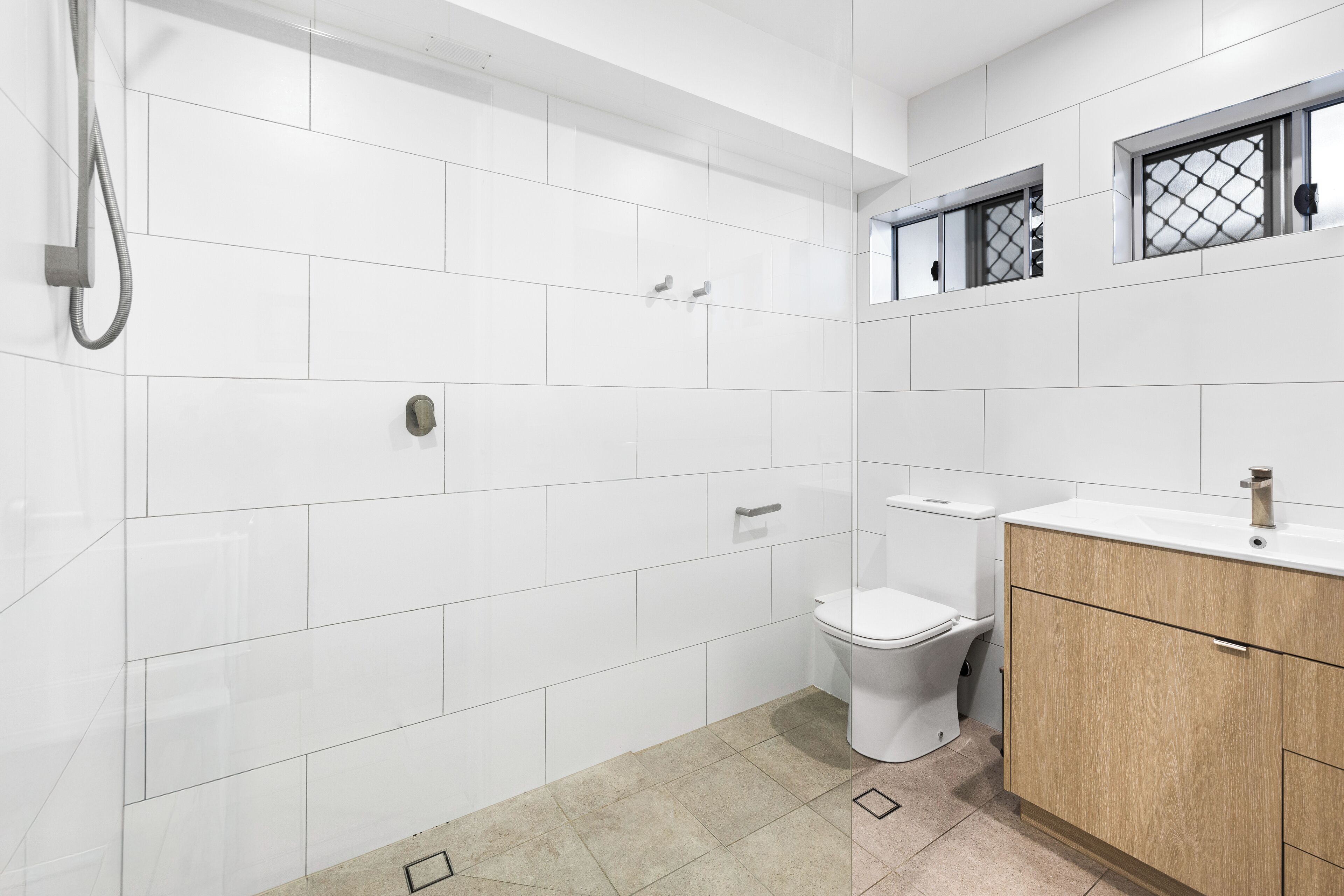 Une salle de bain moderne avec des carreaux blancs, un meuble-lavabo en bois, des toilettes et un espace douche.
