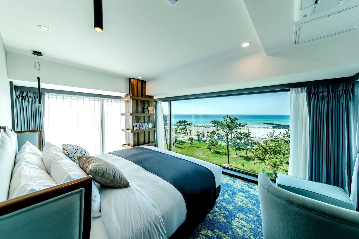 A hotel room with a large bed, a bookshelf, and a view of the ocean.