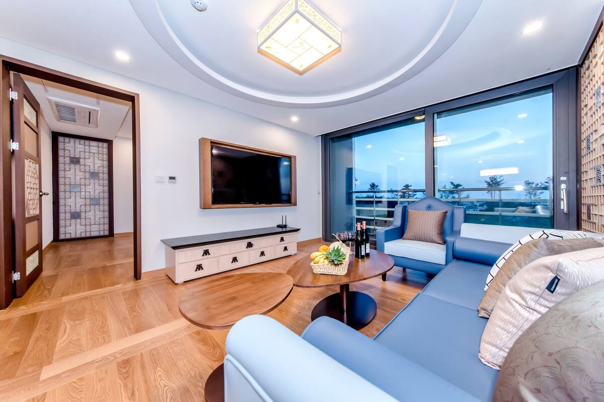 A modern living room with a flat-screen TV, a sofa, a coffee table, and a dining area.