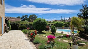 A stone pathway leading to a pool area with a fenced swimming pool, surrounded by lush greenery and flowering plants.