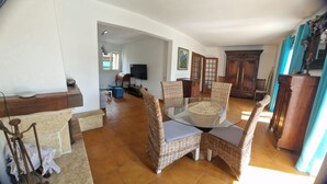 Un salón amplio con una mesa de comedor de vidrio rodeada de sillas de mimbre, un televisor y un gran armario de madera.