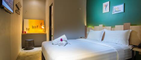 A hotel room with a bed, a small round table, a wall-mounted TV, and artwork.