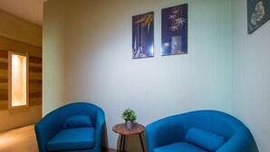 A room with two blue armchairs, a small wooden table with a plant, and two abstract paintings on the wall. - Finess Basic Hotel (Malacca City)