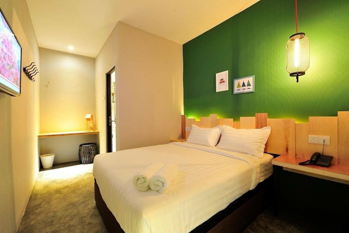 A hotel room with a bed, a desk with a phone, a green accent wall, and a television on the wall.