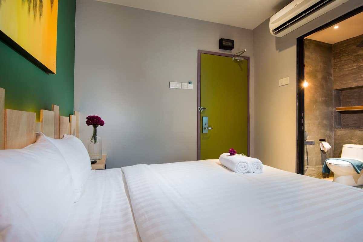 A hotel room with a bed, a nightstand with a vase of flowers, a green door, and a bathroom visible through an open door.