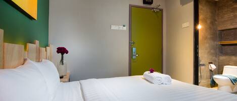 Een hotelkamer met een bed, een nachtkastje met een bloevas, een groene deur en een zichtbare badkamer door een open deur.
