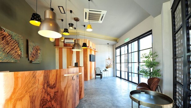 A modern reception area with a wooden reception desk, pendant lighting, and large windows providing natural light. - Finess Basic Hotel (Malacca City)