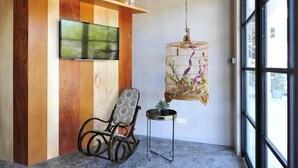 A room with a wooden wall, a mounted TV, a rocking chair, a small table, and a hanging birdcage with flowers. - Finess Basic Hotel (Malacca City)