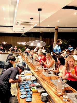 A restaurant with a long wooden counter, multiple tables, and a variety of dishes and drinks. - Blue Lagoon Beach Resort (Nacula Island)
