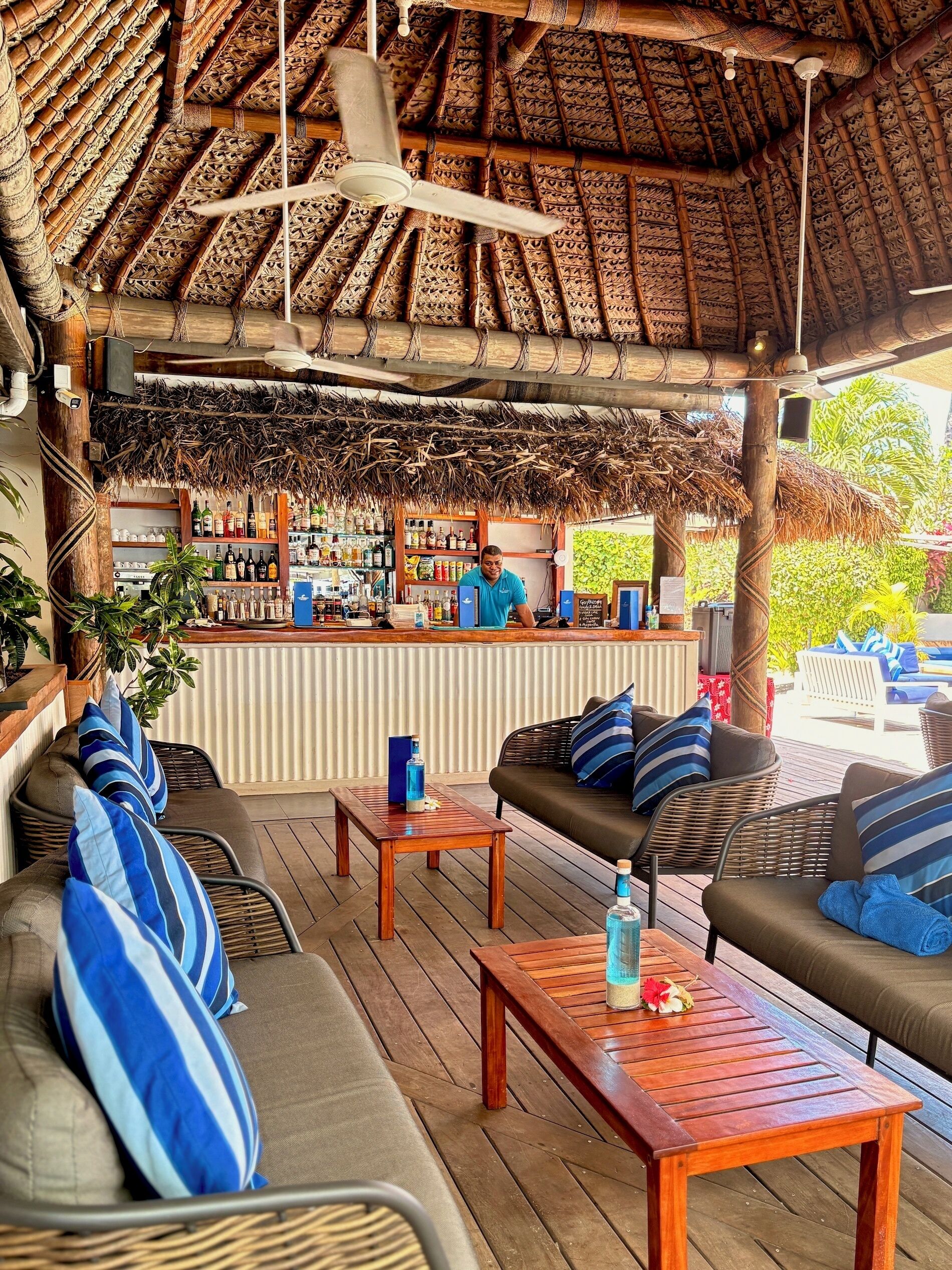 An outdoor bar area with a thatched roof, wooden furniture, and a bar counter stocked with beverages.
