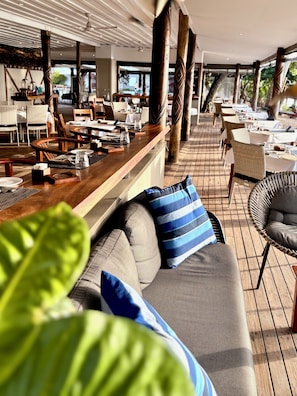 An outdoor dining area with wooden tables and chairs, a bar, and a seating area with cushions. - Blue Lagoon Beach Resort (Nacula Island)