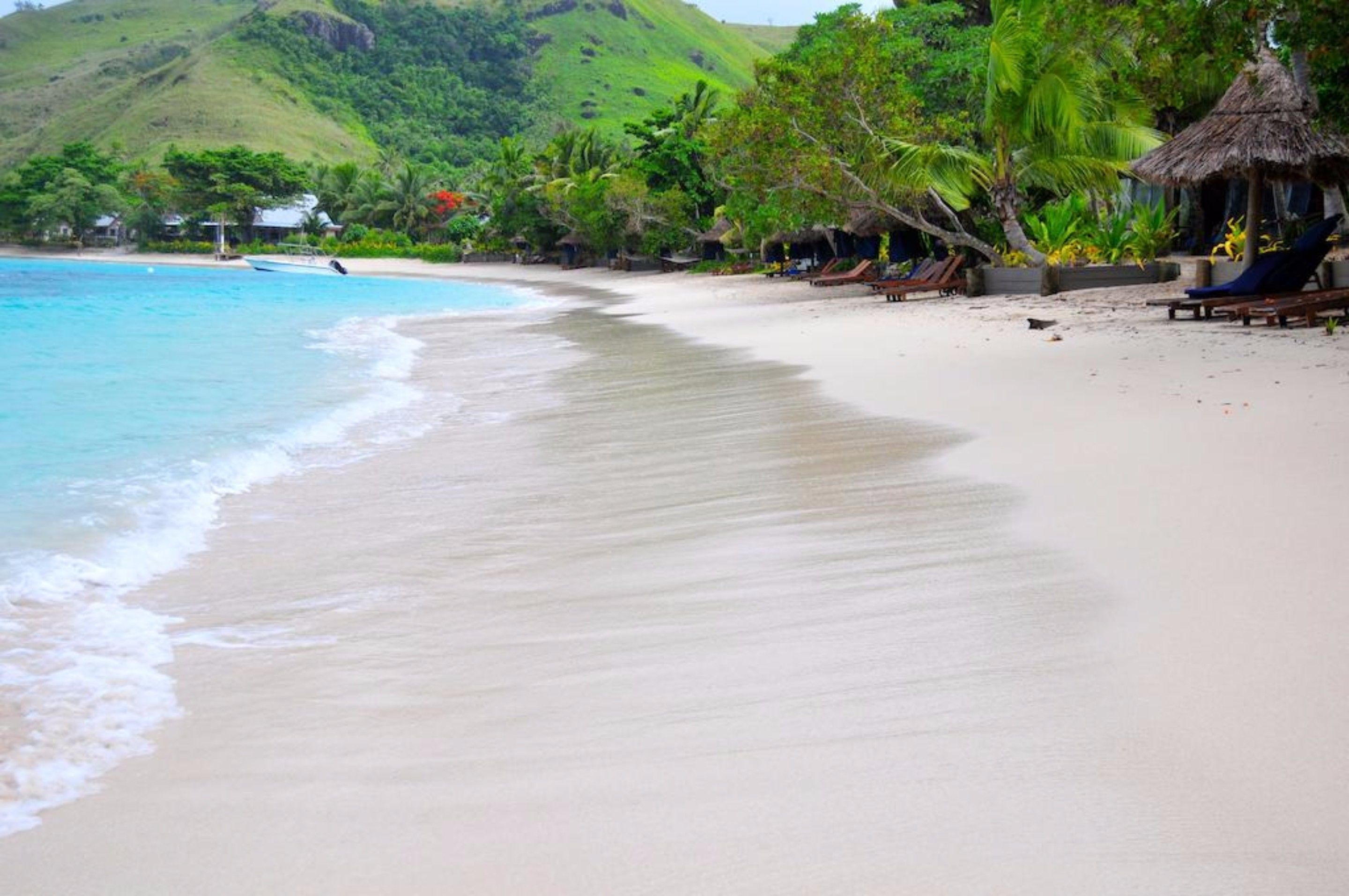 Une plage à l’eau turquoise et limpide, un rivage sablonneux et une cabane à toit de chaume.