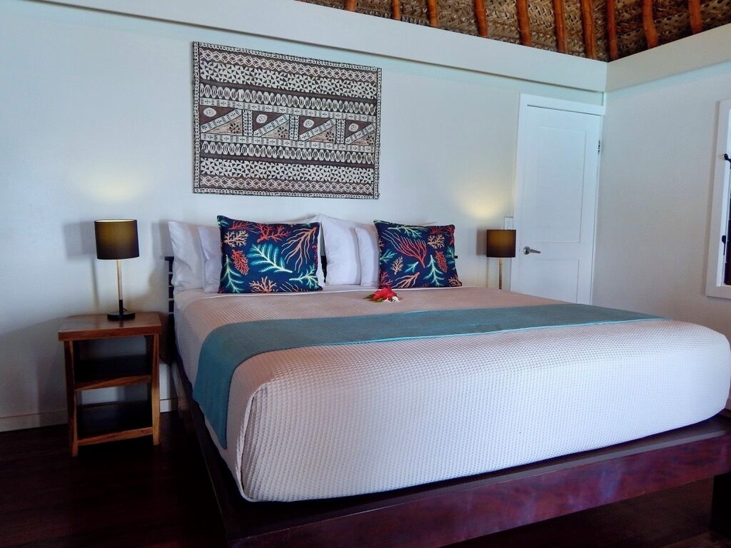 A neatly made bed with a patterned headboard, a small wooden nightstand with a lamp, and a decorative wall hanging above the bed.