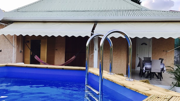 A swimming pool with metal ladders, a covered patio area, and a table with chairs.
