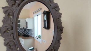 A mirror with an ornate frame reflecting a kitchen area with cabinets, a clock, and a window.