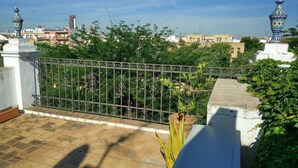 A rooftop terrace with a wrought iron fence, potted plants, and a view of the cityscape.