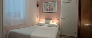 A single bed with a white bedspread in a room with a door and a framed picture on the wall.