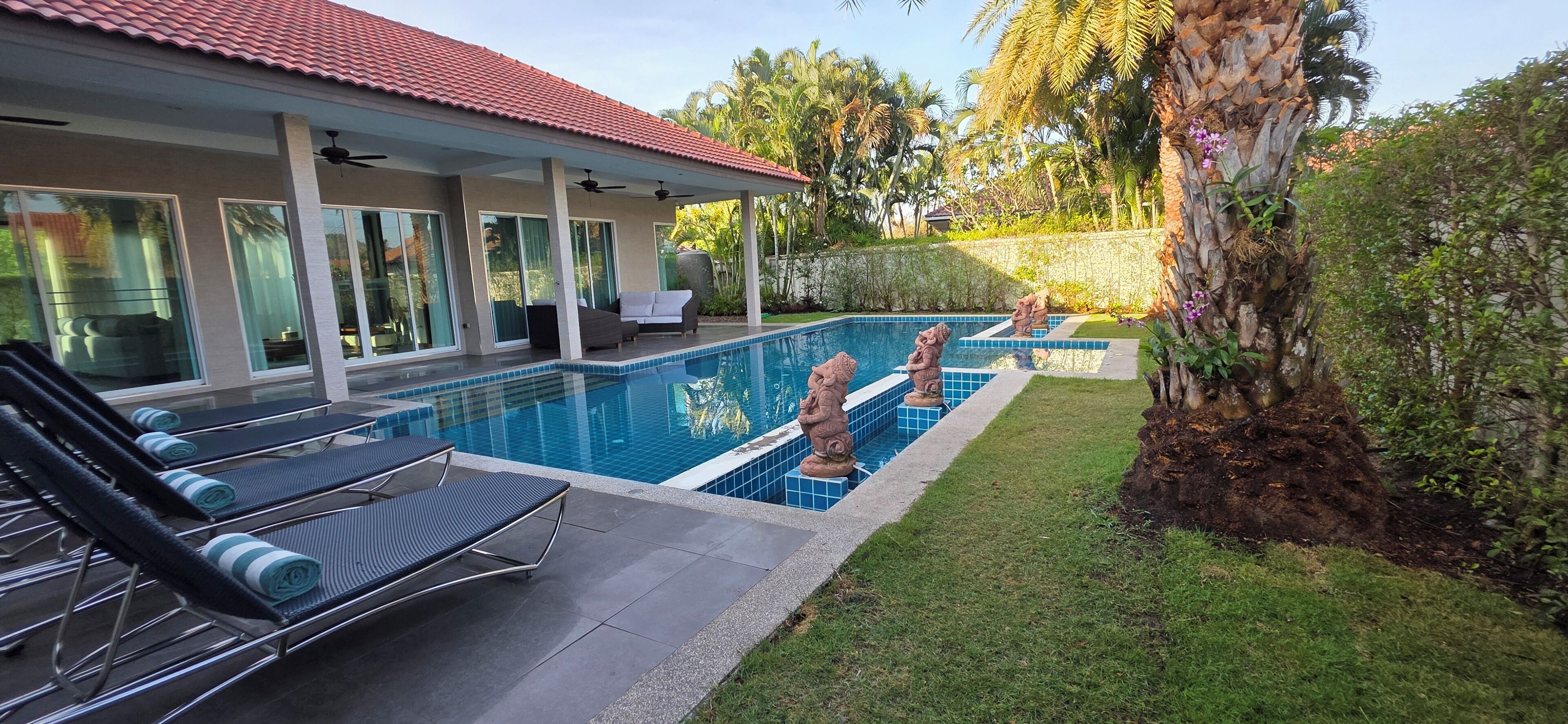 Una piscina con sillas de descanso, un porche cubierto y jardines tropicales.