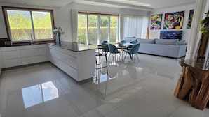 A modern kitchen with white cabinets, a black countertop, and a dining area with blue chairs. - LUXURY HIGH END POOL VILLA   (Tambon Nong Kae)