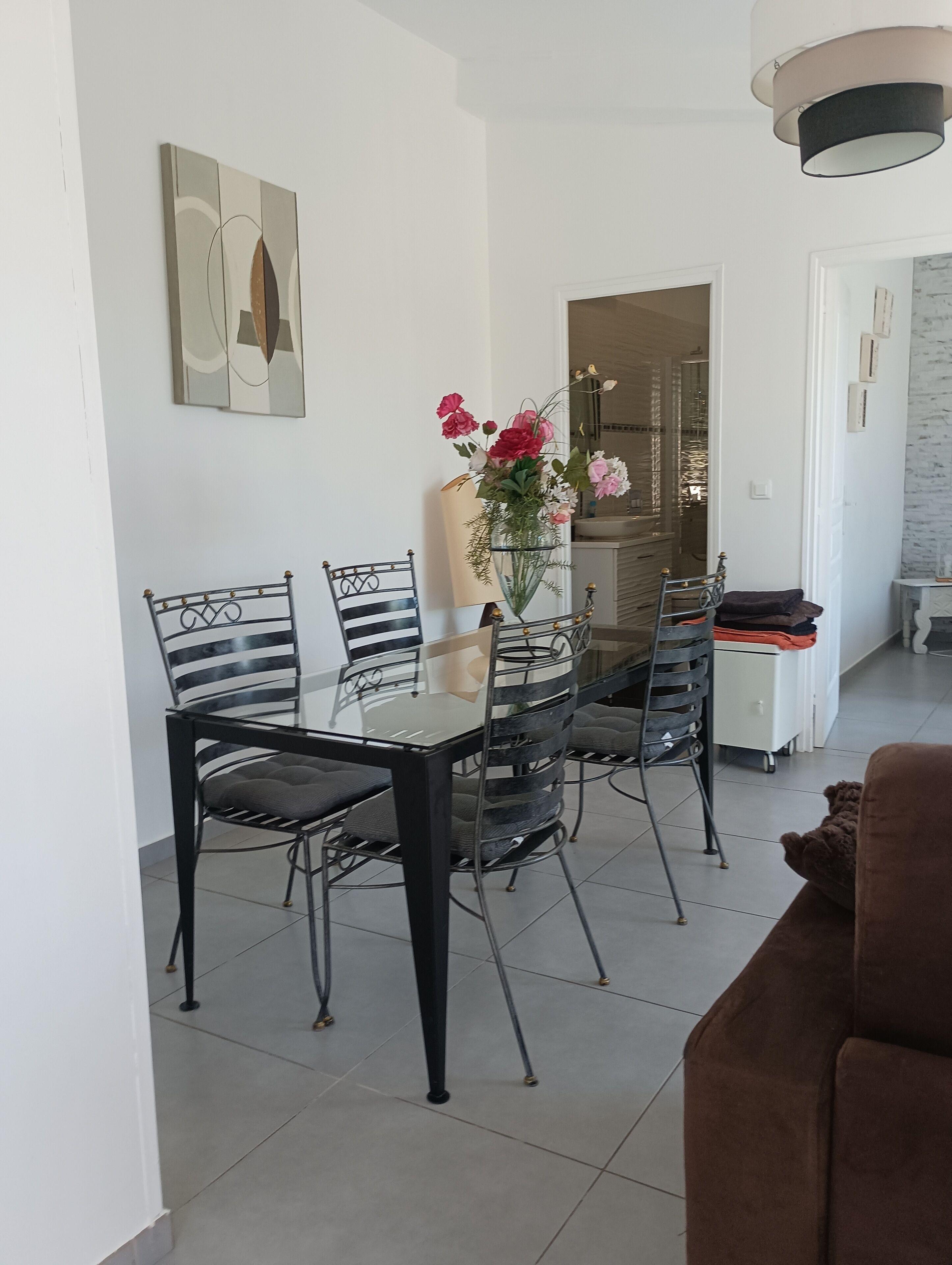 A dining area with a glass table and metal chairs, a vase with flowers, and a modern light fixture.