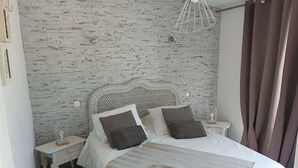Een slaapkamer met een wit bed, een wand met grijs patroon en een witte nachtkastje met een lamp.