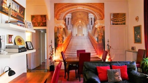 A living room with a black leather sofa, red cushions, a dining table with chairs, and a staircase leading to an upper level. - "Diva"' apartment with unique atmosphere in a prime location (Nîmes)