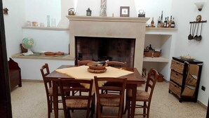 A dining area with a table set for four, a fireplace, and shelves with various items.