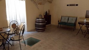 A room with a dining table, chairs, a sofa, a large barrel, and a small table with a lantern.