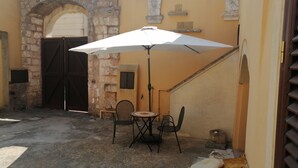 An outdoor seating area with a table and chairs under a white umbrella, a stone wall, and a closed wooden gate.
