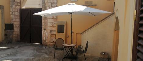 An outdoor seating area with a table and chairs under a white umbrella, a stone wall, and a closed wooden gate.