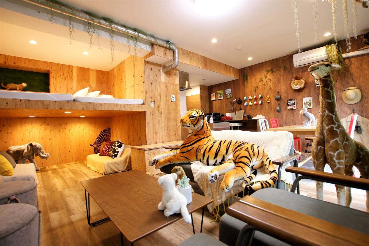 A room with wooden walls, a sofa, a table, and various stuffed animals including a tiger, giraffe, and a dog.