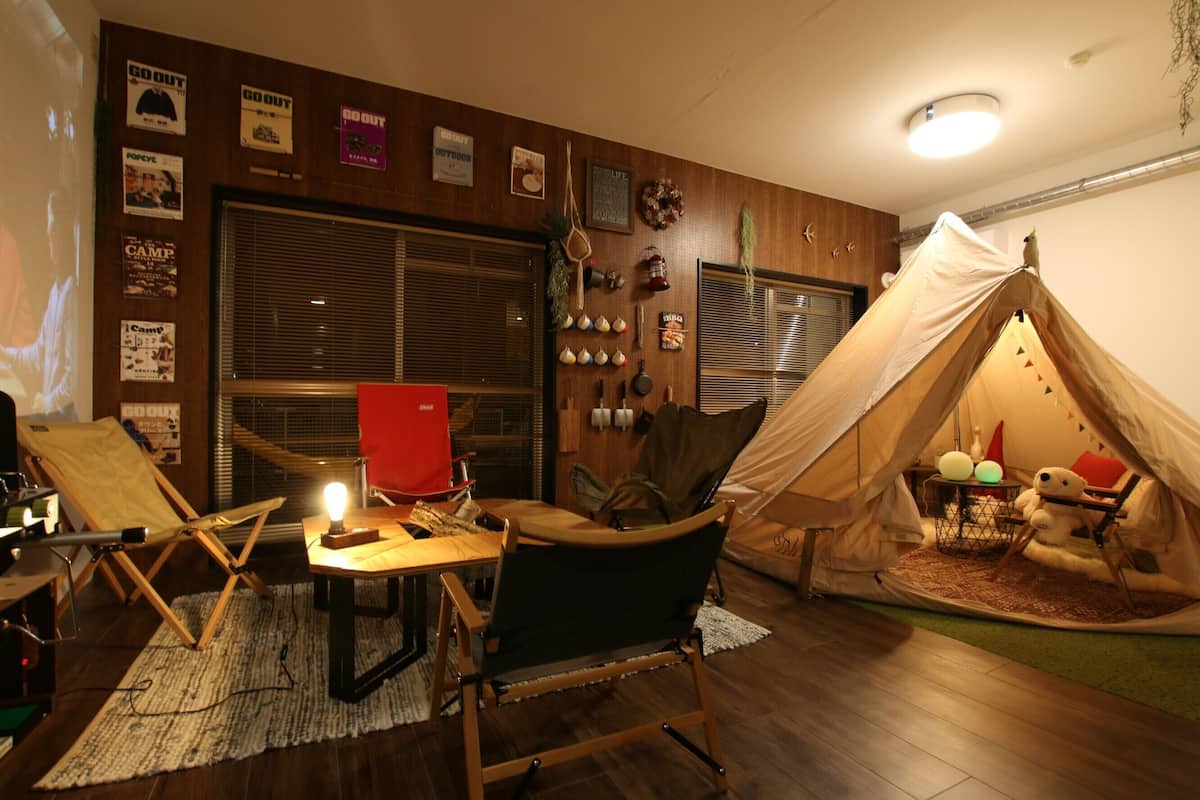 A cozy room with a tent, a wooden table, a red chair, and various posters on the wall.