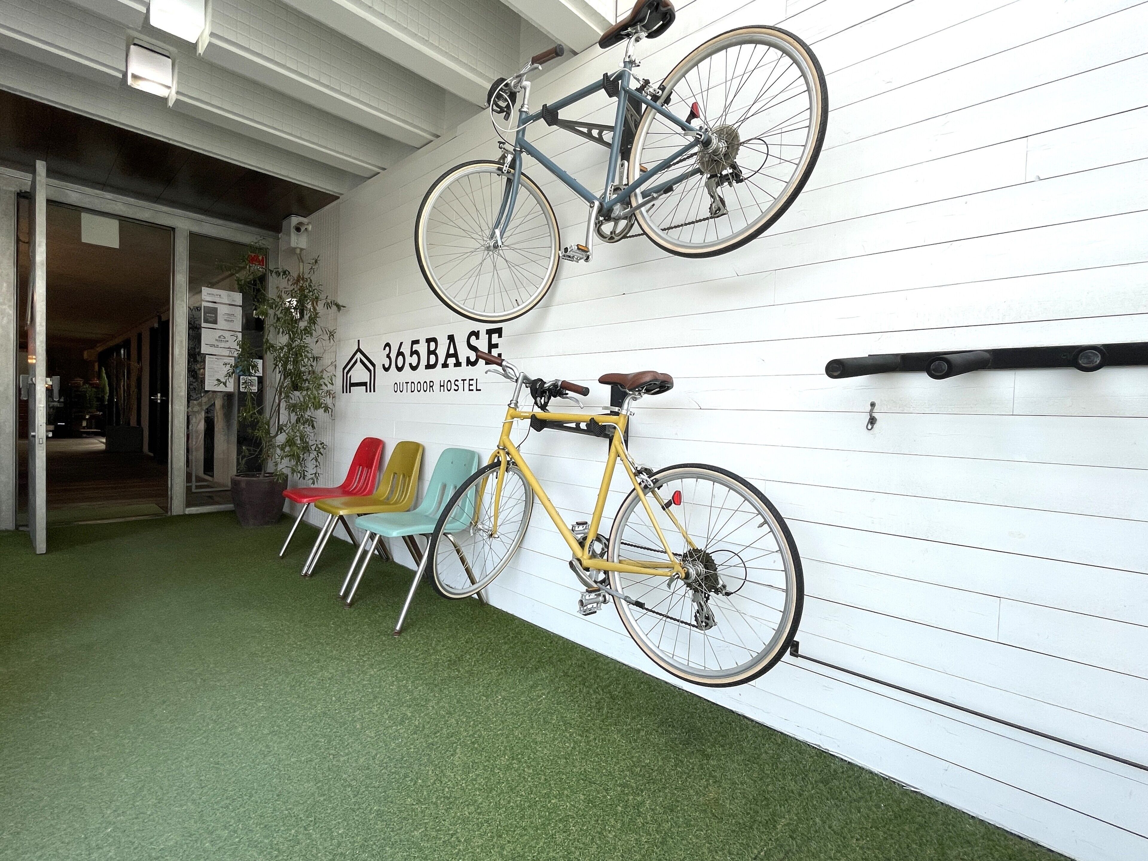 Ein Zimmer mit weißer Wand, einem gelben Fahrrad und bunten Stühlen.
