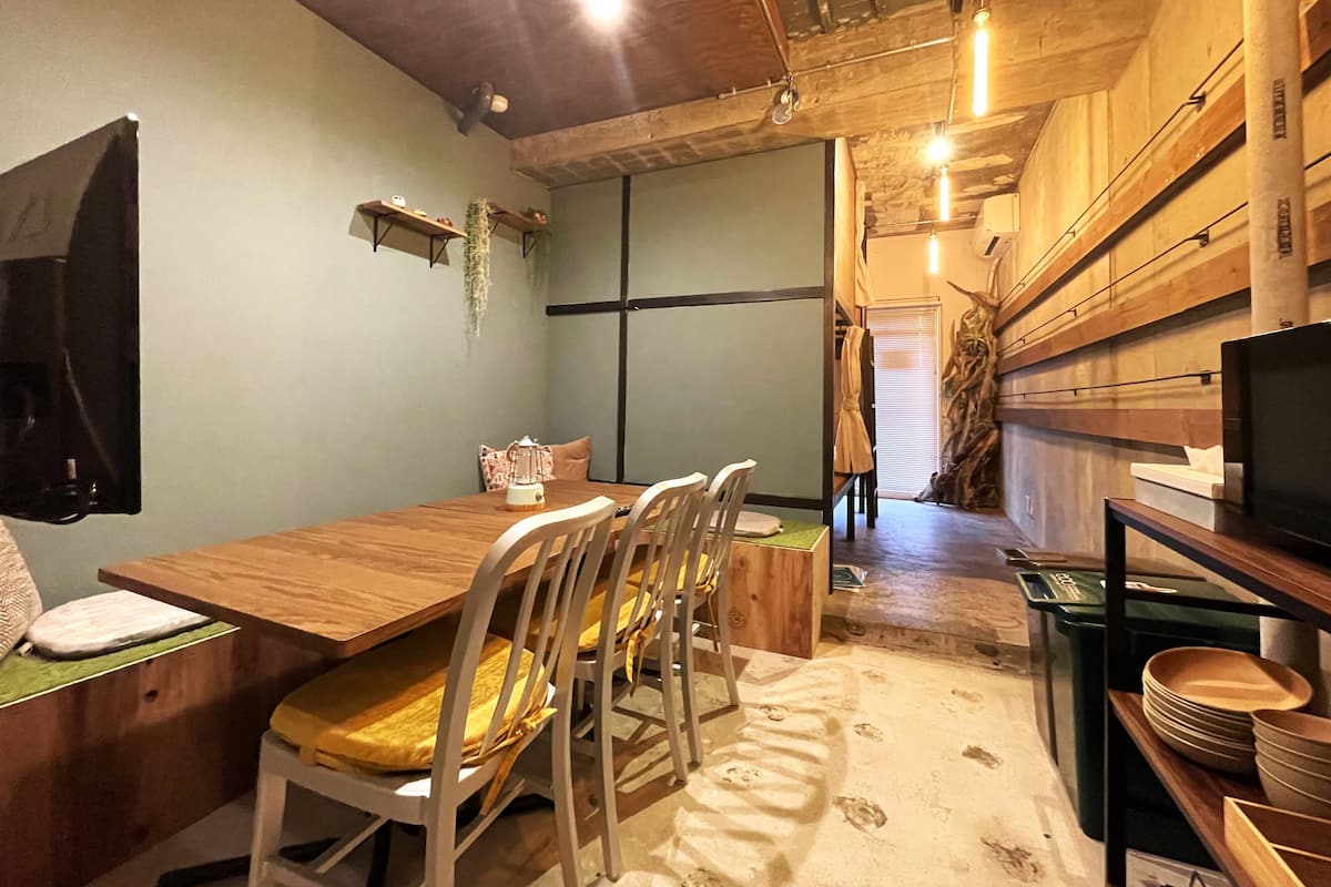 A dining area with a wooden table and chairs, a television on the wall, and a staircase leading to another level.