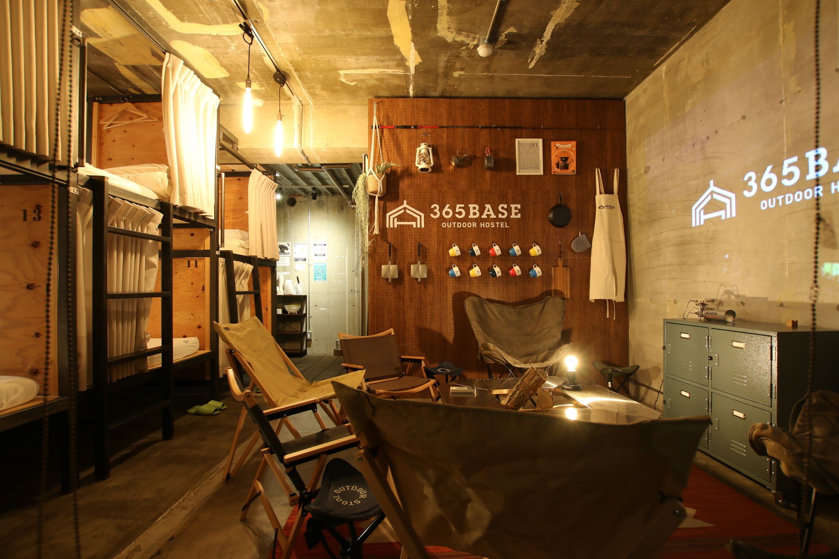 A rustic indoor setting with bunk beds, a wooden wall with a sign, and a table with chairs.