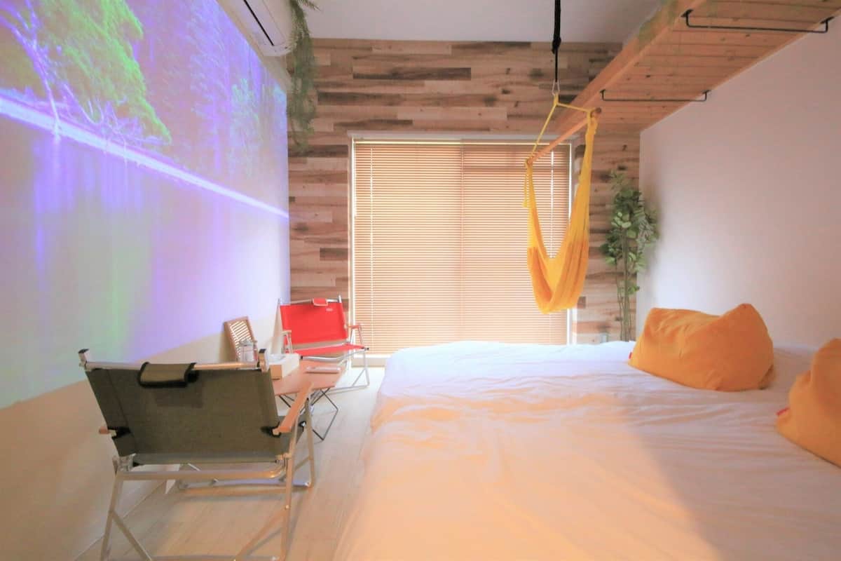 A room with a bed, a projector screen, a hanging chair, and a window with blinds.