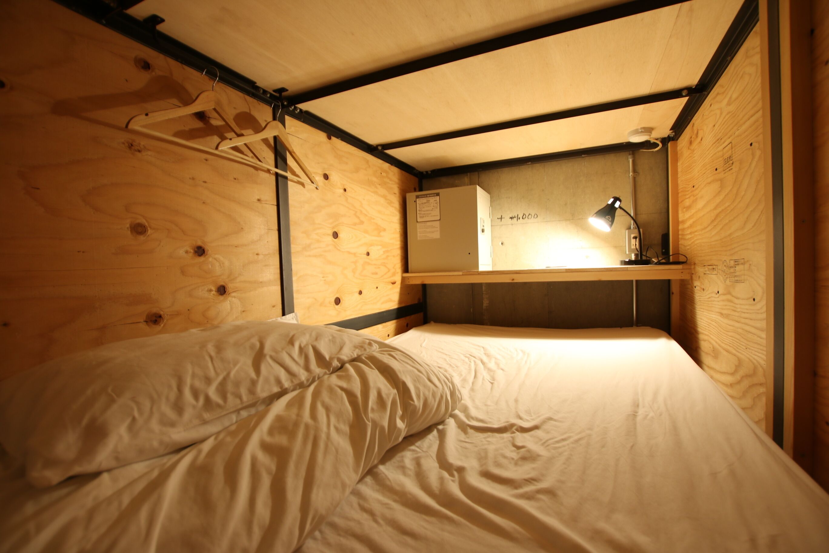 Una habitación pequeña y funcional con una cama nido, un escritorio con lámpara y un mueble auxiliar.