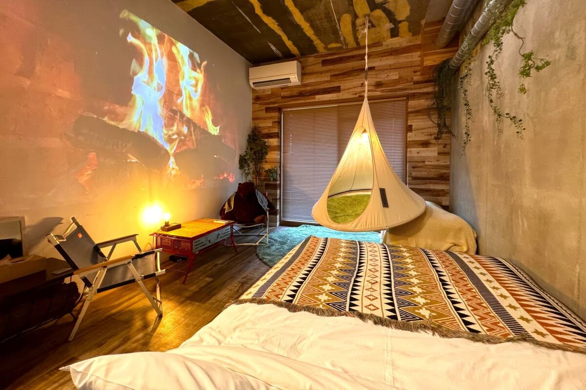 A cozy room with a projector displaying a fire, a hanging chair, a bed with patterned bedding, and a wooden ceiling.