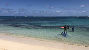 A beach with clear turquoise water, a sandy shore, and several boats in the distance.