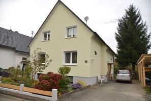 A two-story house with a sloped roof, satellite dish, and a car parked in the driveway.