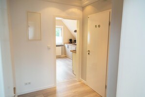 A hallway leading to a kitchen with a window, a door with a lock, and a power outlet on the wall.