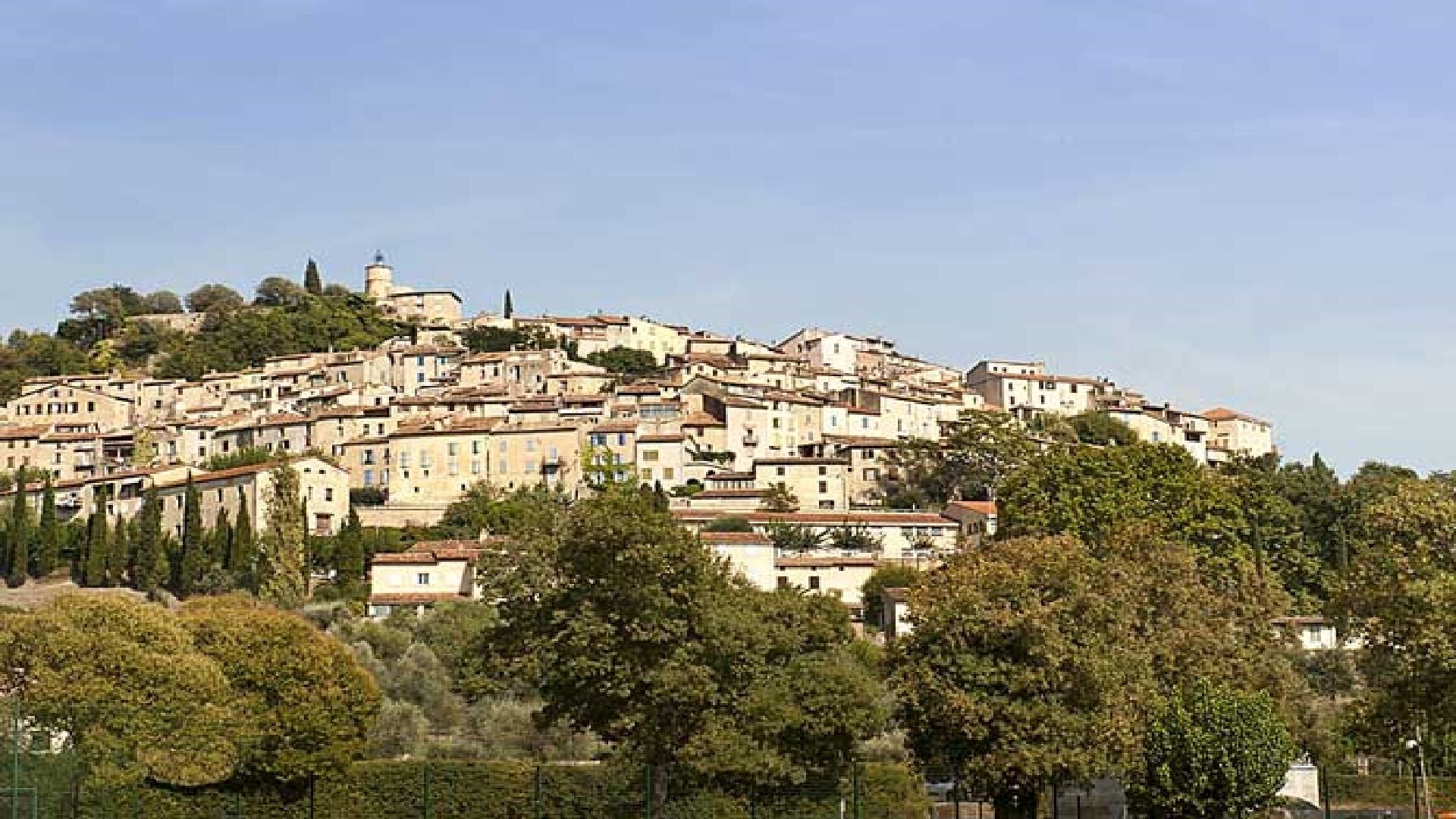 A densely packed hillside town with historic buildings, surrounded by trees and a clear sky.