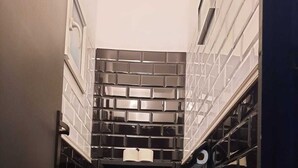 Une petite salle de bain comprenant des toilettes, une étagère avec du papier toilette et un pare-feu noir en carreaux.