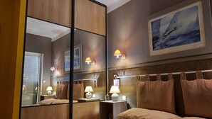 Une chambre d’hôtel avec un grand miroir, un tableau représentant un voilier et un lit avec de nombreux oreillers.
